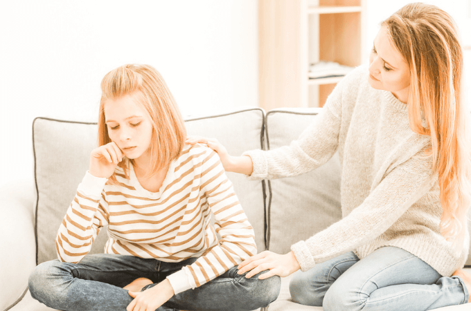 image of mother comforting tween aged girl on their sofa at home