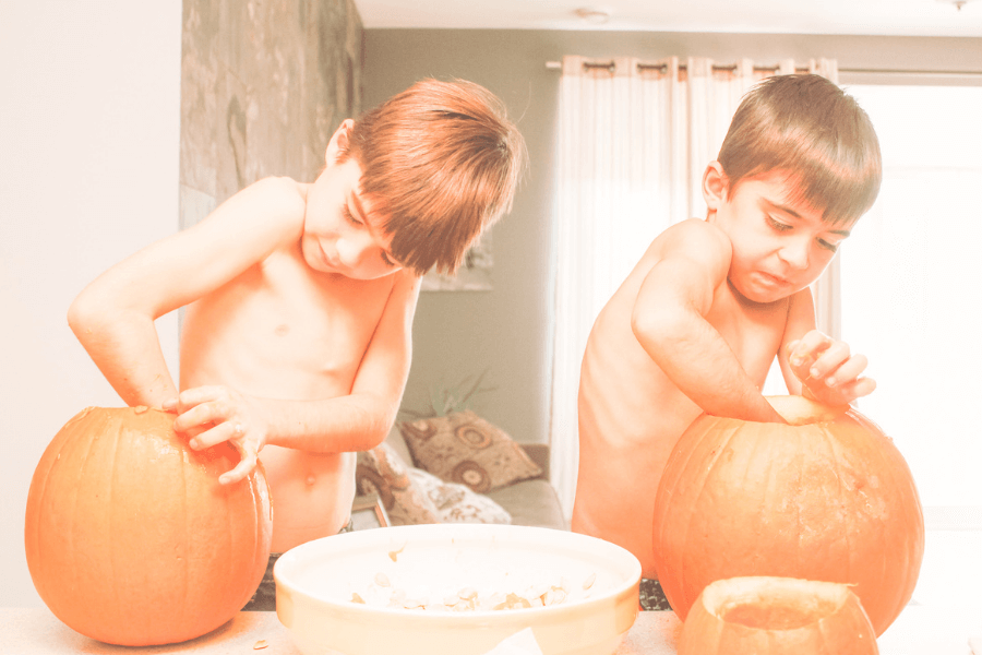 image of two young boys scooping seeds out of pumpkin to make Halloween pumpkin; idea of Halloween family traditions