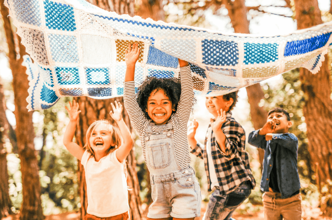 Image of four young children outdoors in a forest carrying a beautiful quilted blanket overhead - suggesting the concept of executive functioning skills.