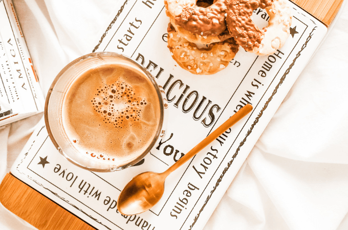 image of a creative coffe drink - possibly a caramel latte - along with a bakery treat a spoon and a newspaper