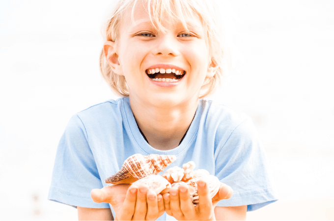happy young boy on beach with hands filled with shells
