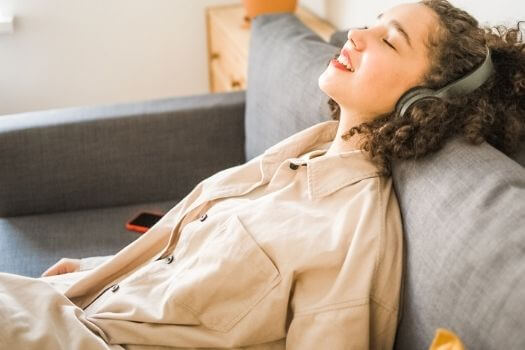 young teen relaxing back on couch while listening to music on headphones